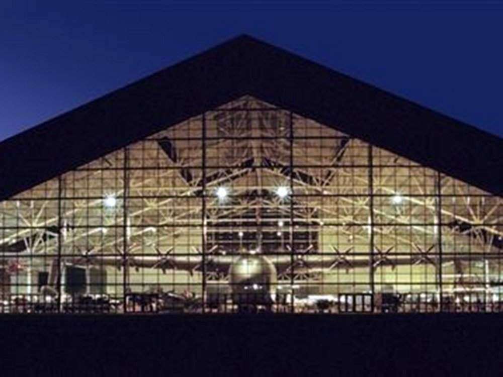 A large hangar with a triangular glass facade showing the silhouette of a large aircraft inside, a unique stop for day trips near Willamette Valley.
