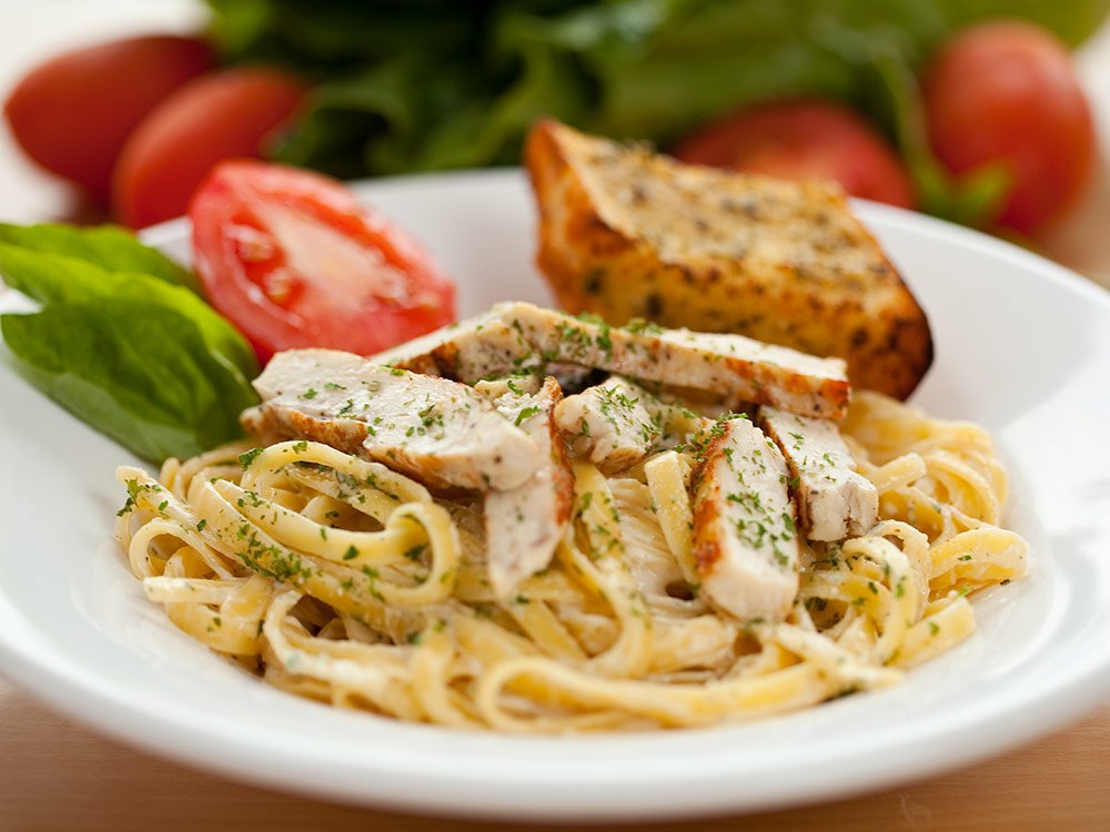 Fettuccine Alfredo topped with sliced grilled chicken, served with a tomato wedge and garlic bread at one of the top restaurants in Yamhill County.