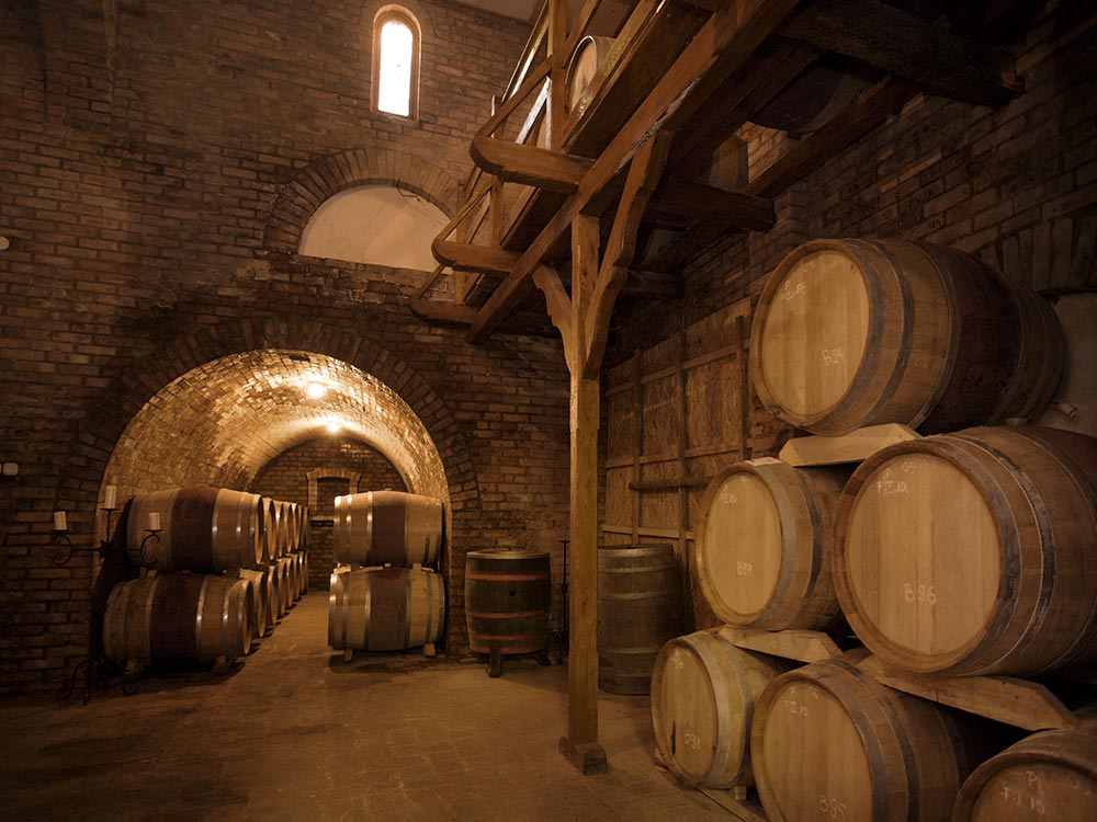 Wooden wine barrels stacked in a rustic, arched brick cellar at one of the Willamette Valley wineries and tasting rooms.