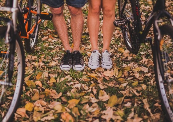 Two people standing on fallen leaves between their bicycles.